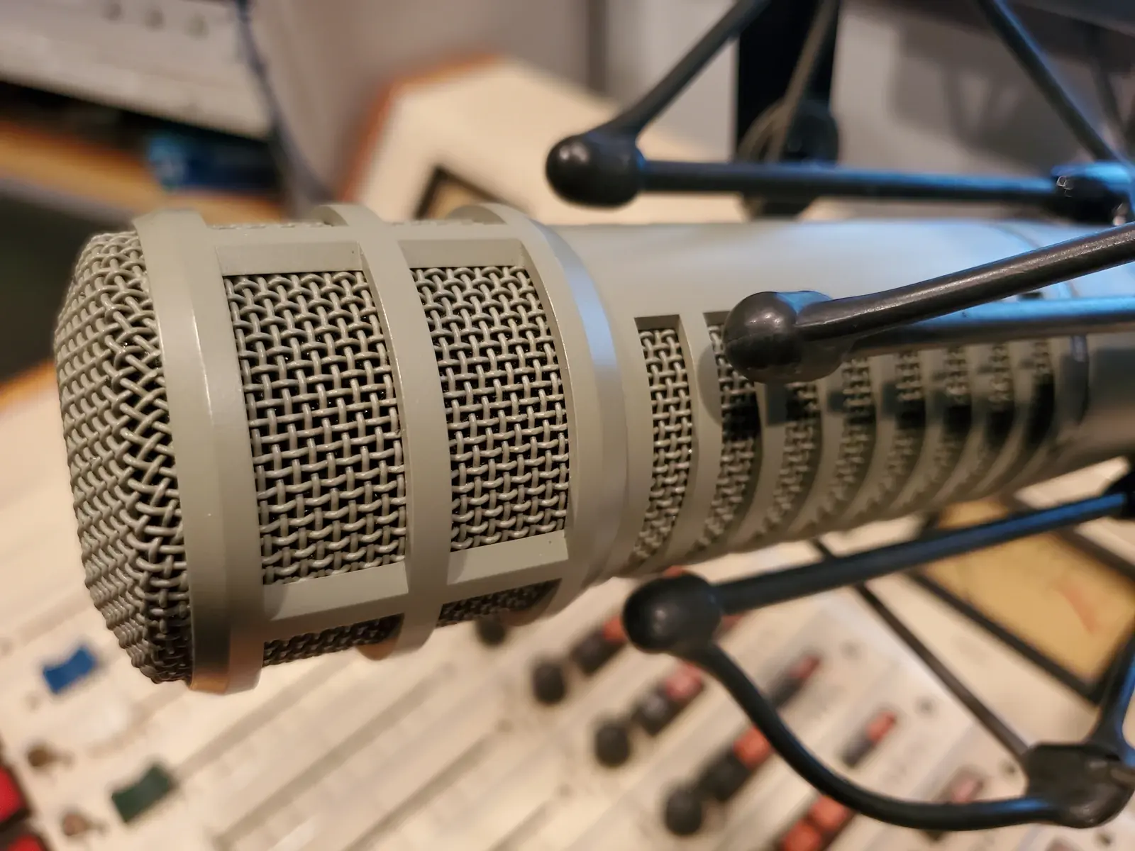 Broadcasting mic — a studio microphone on its boom arm, close up, with the mixing board behind it