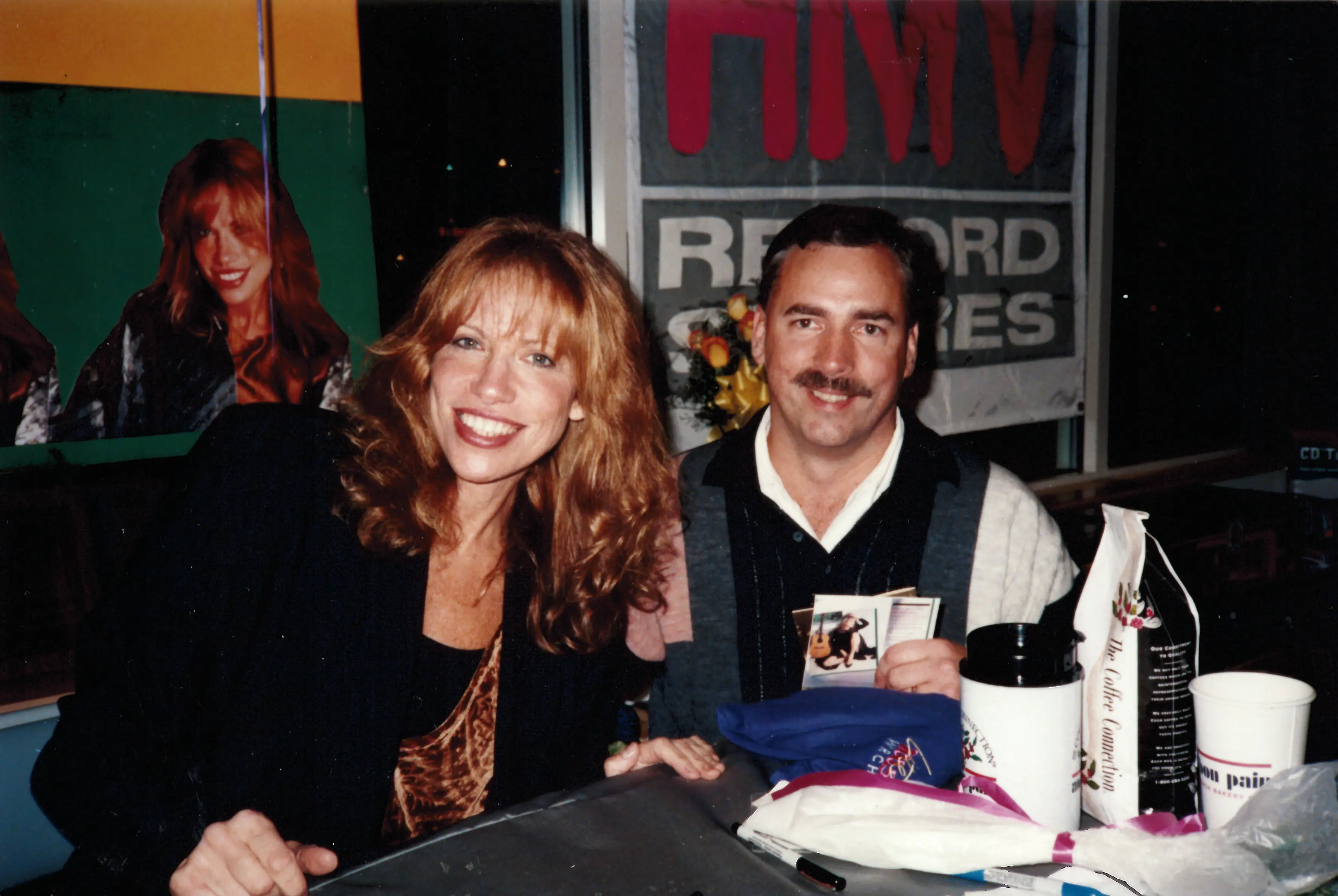 Allan Camp with a recording artist at an HMV Record Stores in-store appearance, seated together behind a signing table